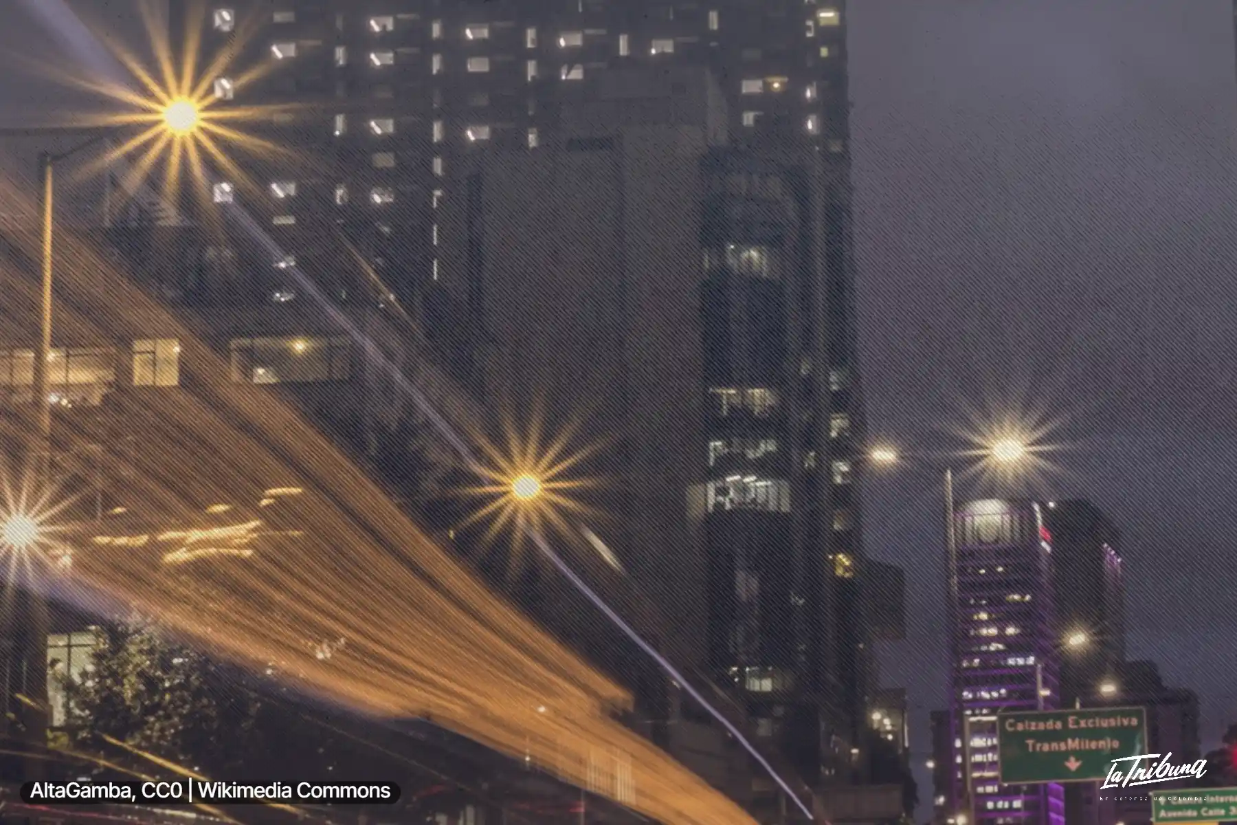 Panorámica nocturna de Bogotá con edificios altos, luces de la vía y estelas del tráfico