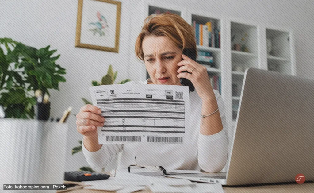 Mujer preocupada habla por teléfono mientras sostiene un recibo del impuesto predial